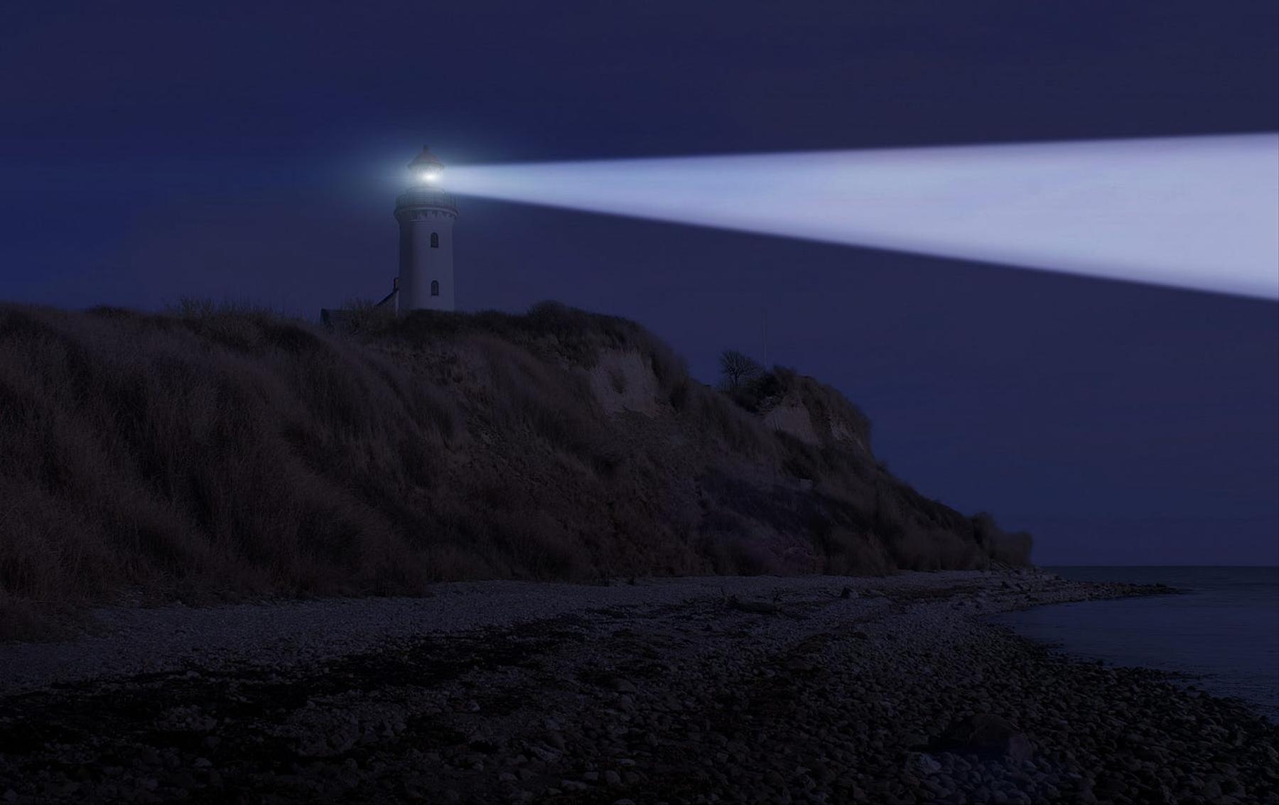 Lighthouse on a hilly shore shining out over a body of water